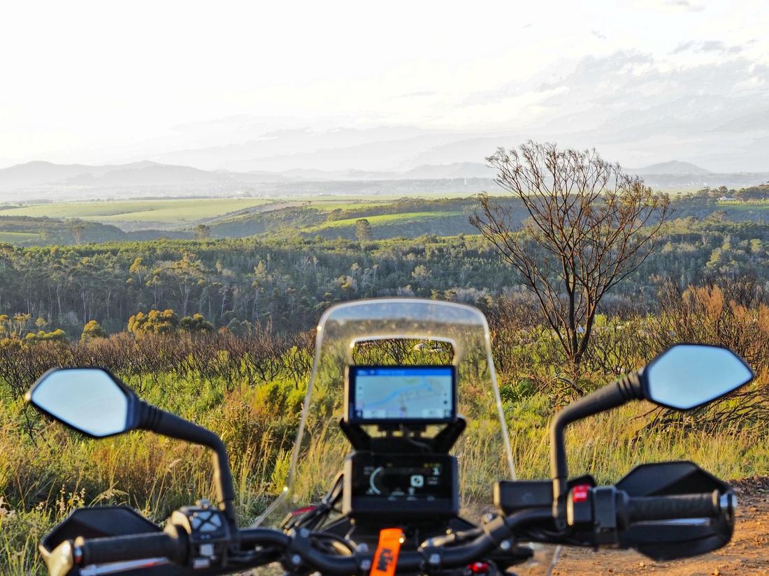 Rider's-eye view from the cockpit of a KTM 790 Adventure, GPS route loaded, overlooking the Eastern Cape valley and forest